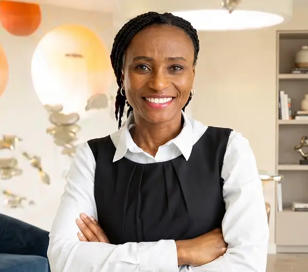 Professional studio portrait of a smiling woman with braided hair, standing with her arms crossed in a white shirt and black sleeveless top.
