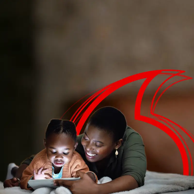 A mother and young child lying down together, smiling while looking at a tablet screen.