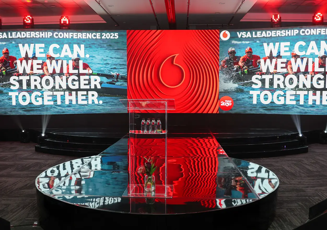Clear podium on a glossy stage set up for the VSA Leadership Conference 2025, featuring large red screens with the Vodafone logo and the slogan "WE CAN. WE WILL. STRONGER TOGETHER."