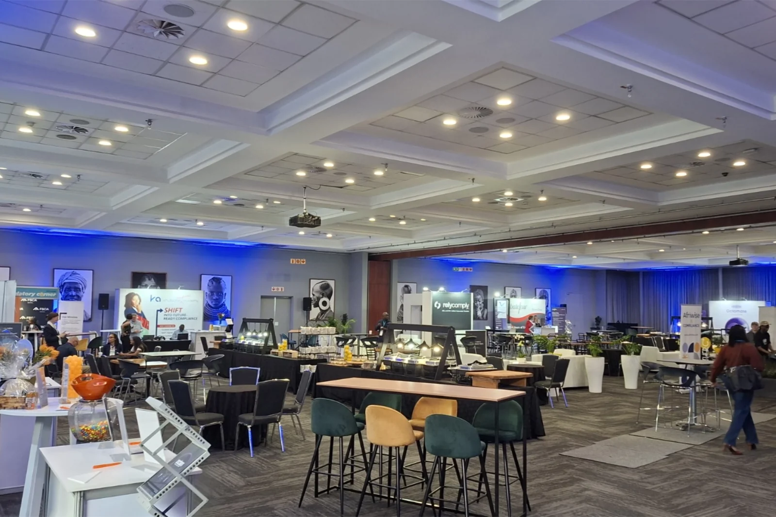 Large exhibition hall set up with corporate sponsor booths, catering tables, and networking seating areas